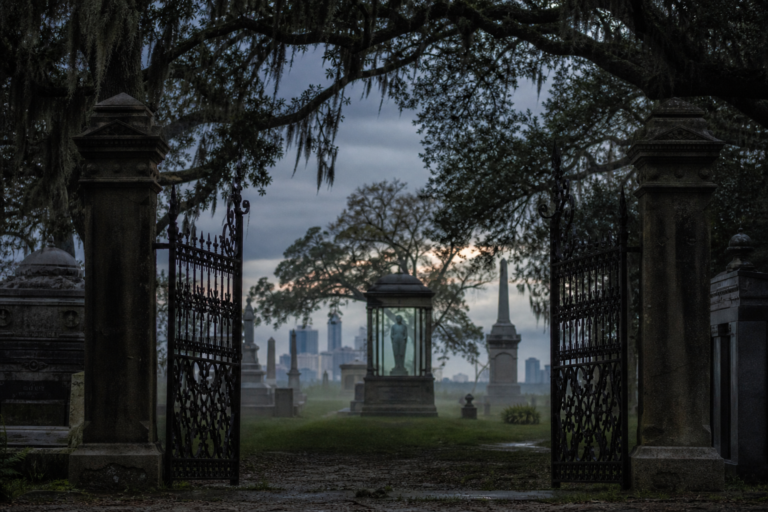 Wrought-iron cemetery gates at dusk with mist, old monuments and a hazy Chicago skyline beyond