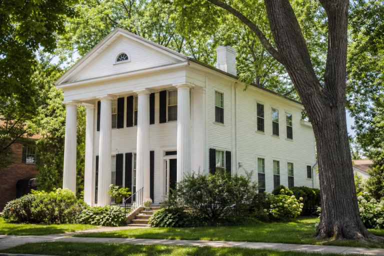 A white 1830s farmhouse with a columned porch among mature trees
