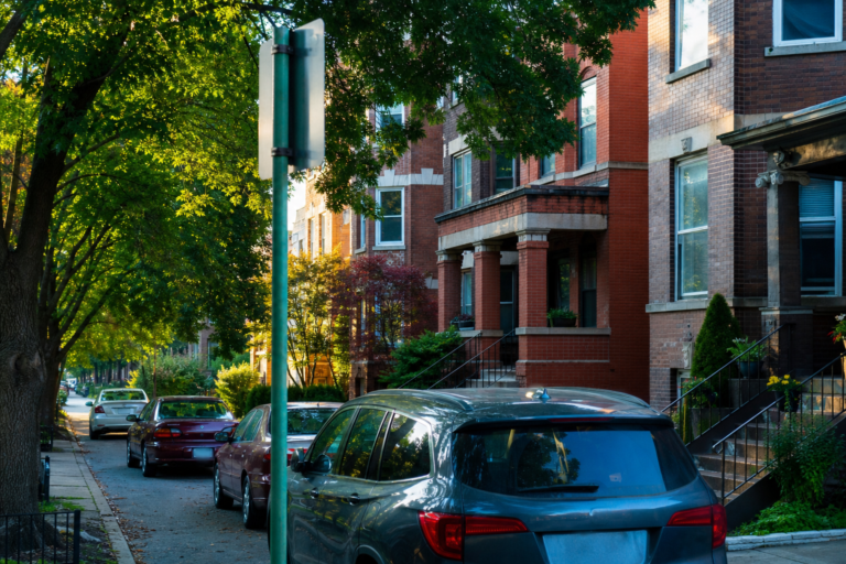 A Chicago side street lined with parked cars and a parking sign pole