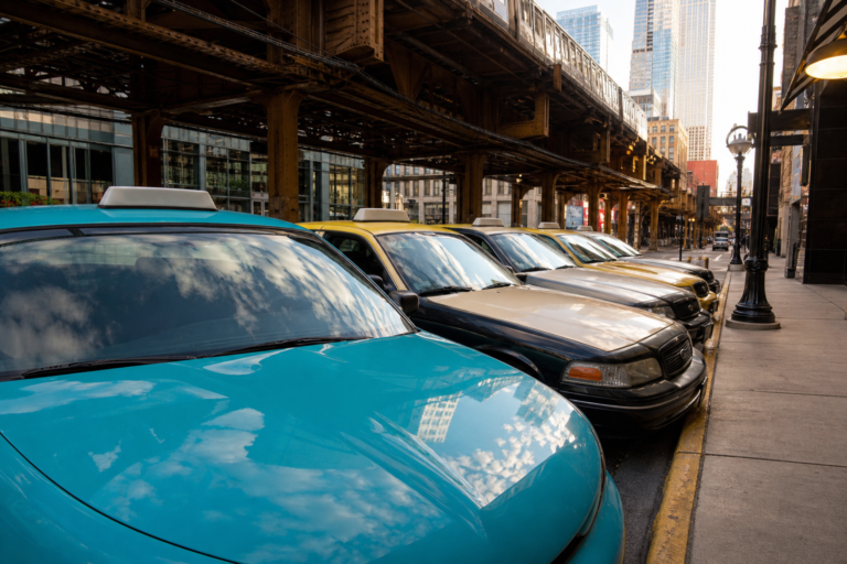 Parked Chicago taxis on a side street beneath elevated train tracks on an overcast day