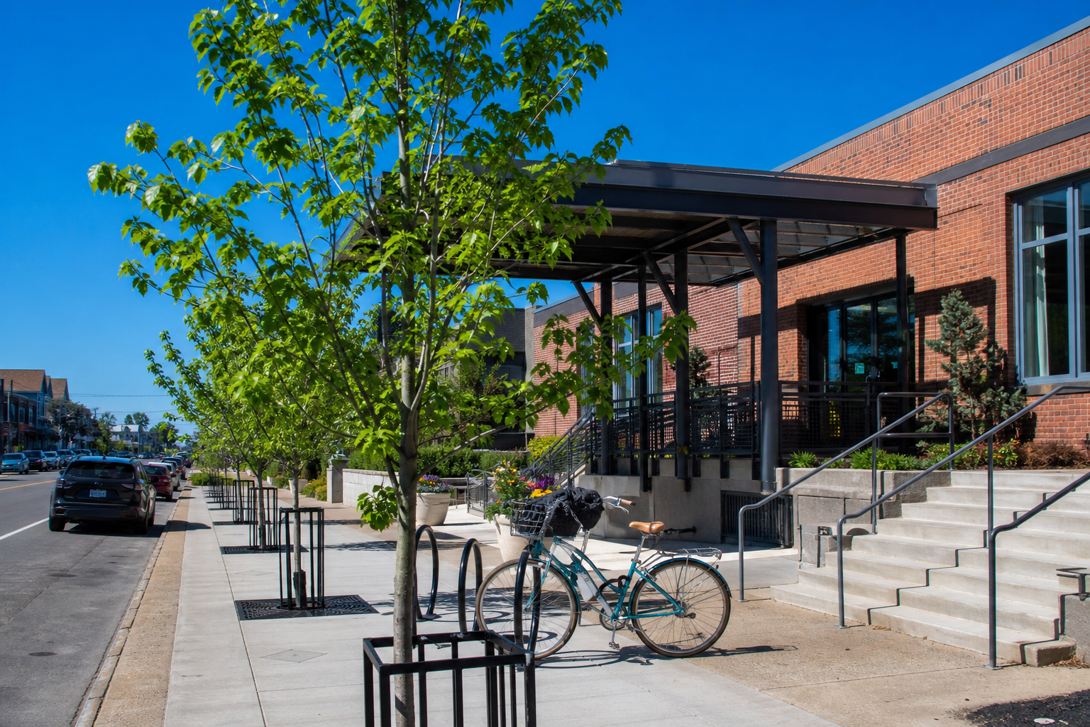 A brick community center with a new sidewalk and young trees on a sunny day