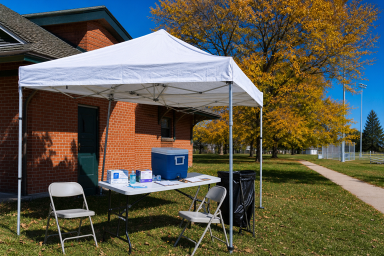 A pop-up clinic tent with a folding table, a vaccine cooler and boxes of bandages in a city park