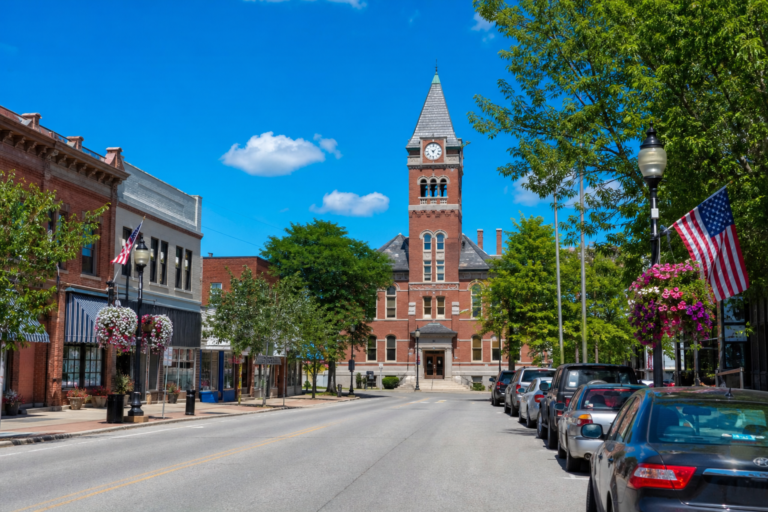 A small-town main street leading to a brick city hall on a bright summer day