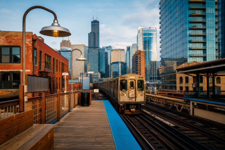 A train arriving at an elevated Chicago L platform with downtown towers behind
