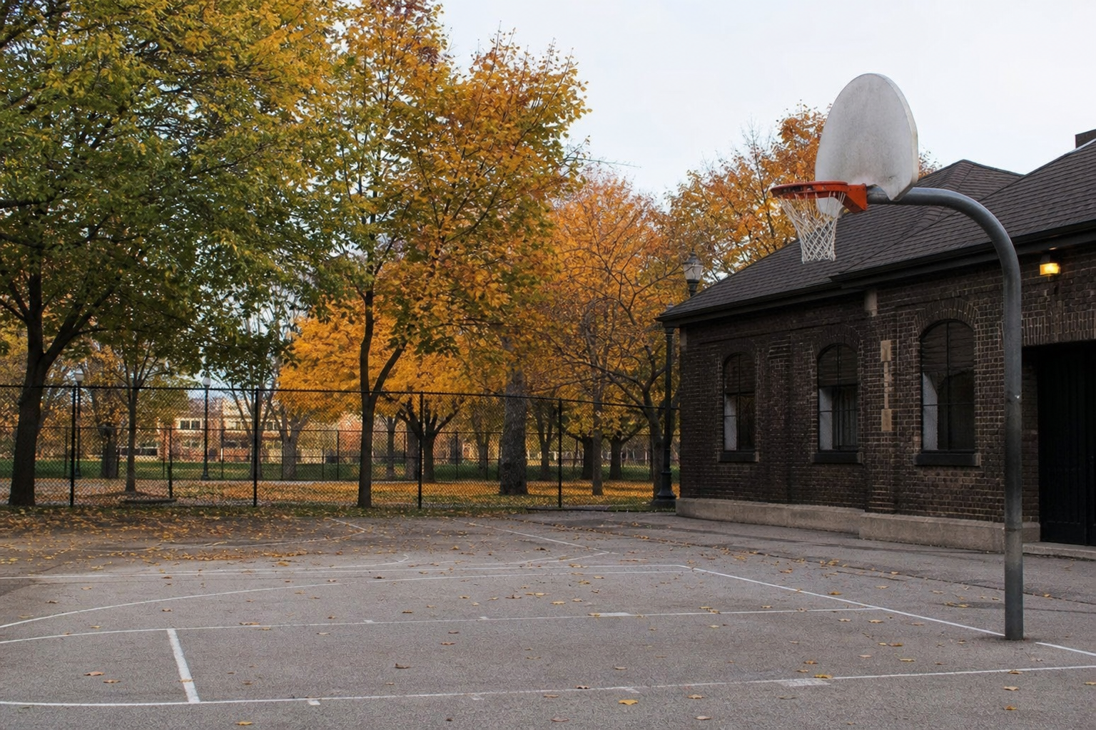 An empty basketball court beside a brick park field house in early autumn