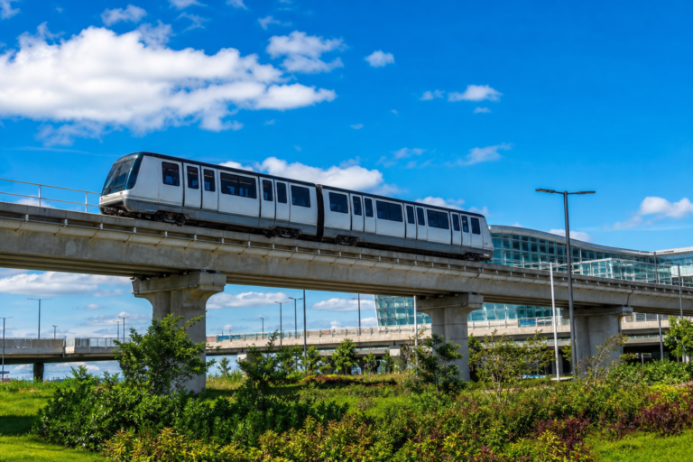 An airport people-mover train on an elevated guideway in bright sunshine
