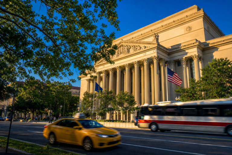 A columned civic building in golden afternoon light with a taxi passing