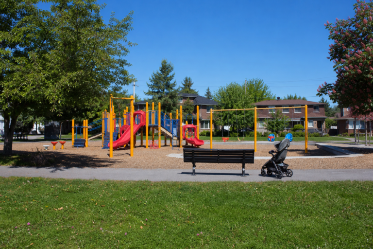A colorful suburban playground with a stroller by a bench on a sunny morning