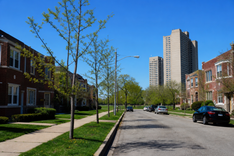 Mid-century apartment towers beyond brick townhomes and lawns on a level street
