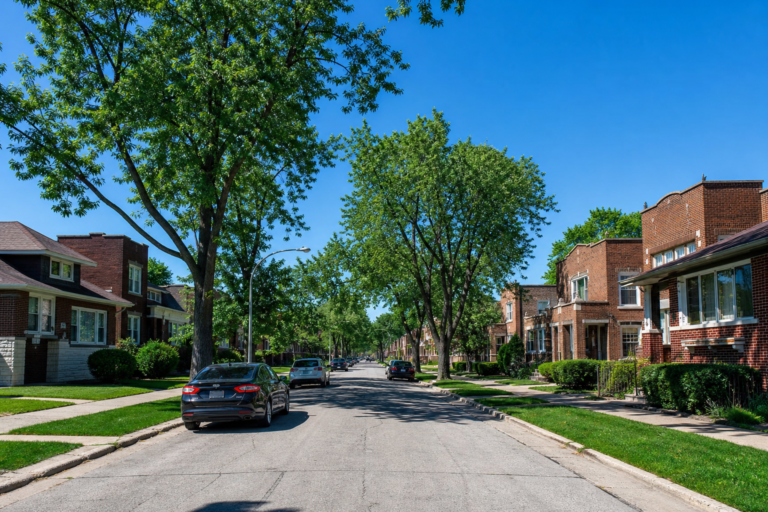 Brick bungalows and two-flats with front lawns on a level, tree-lined street