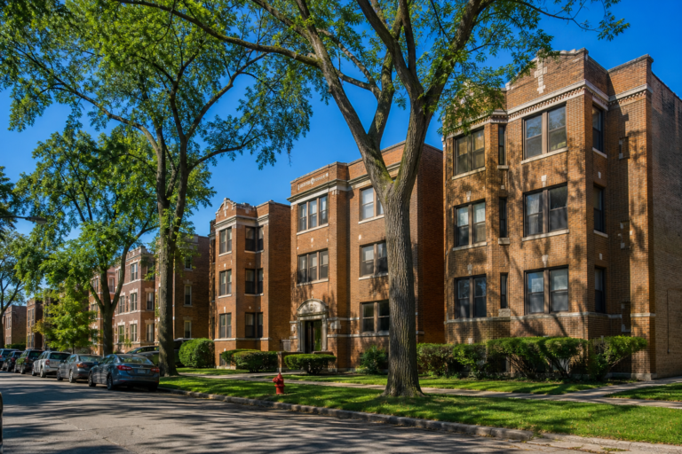Brick courtyard apartment buildings and three-flats on a level, tree-lined street
