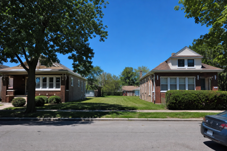 Brick bungalows and frame houses on a level street, with a mowed grassy lot between them