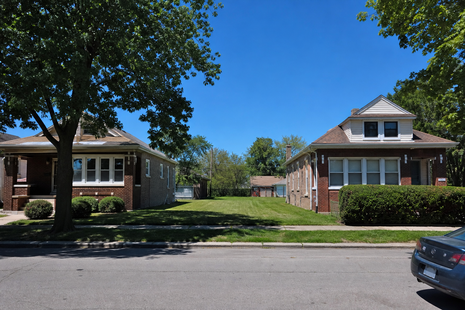 Brick bungalows and frame houses on a level street, with a mowed grassy lot between them