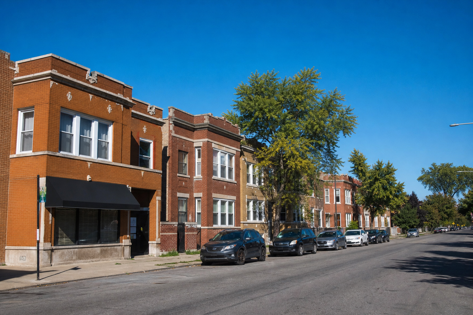 Brick two-flats and three-flats on a level street with a brick corner building and its awning